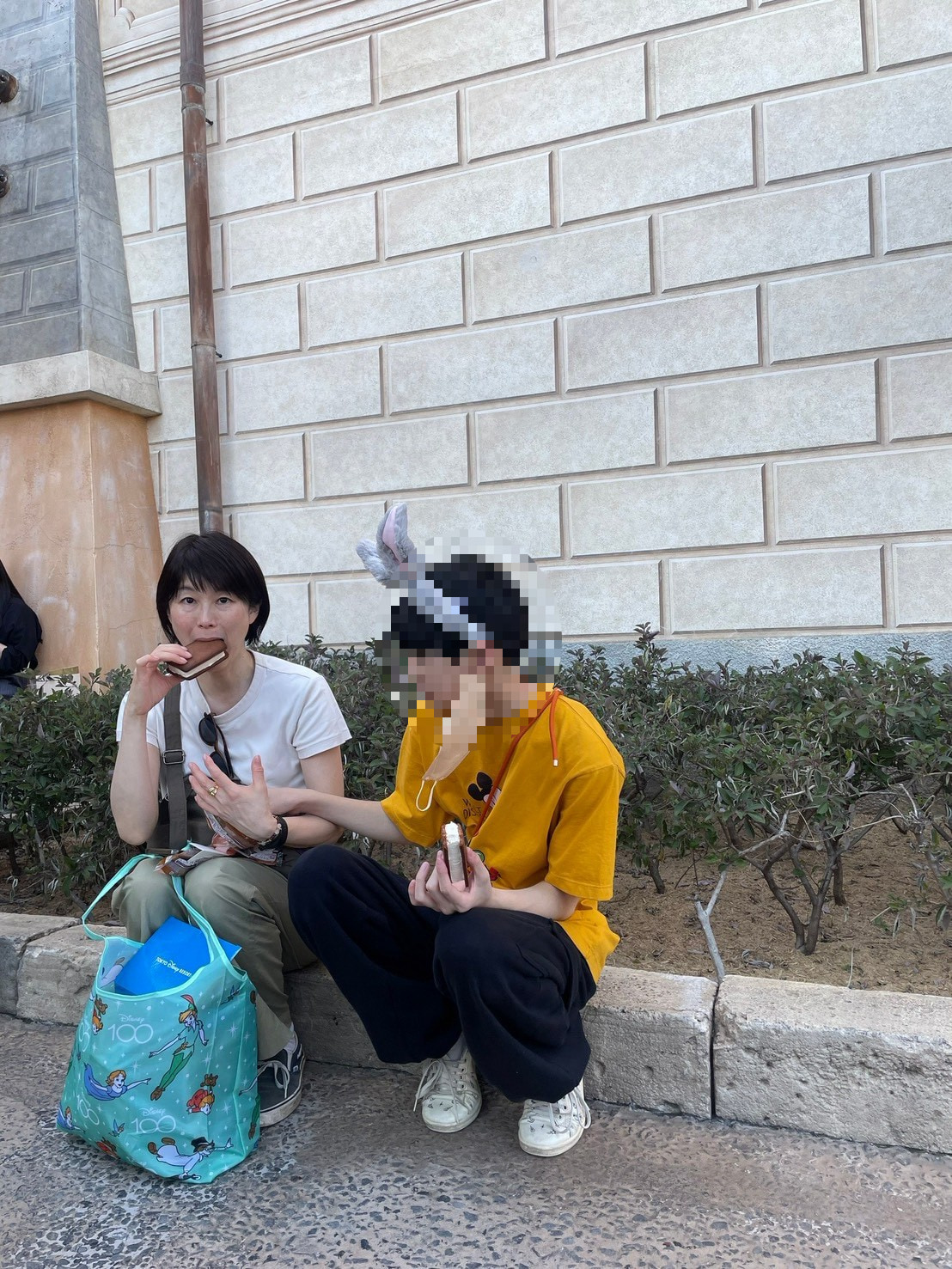 修学旅行の日、ディズニーランドの外で並んで座るやよいさんと息子さん。息子さんの頭部はプライバシー保護のためモザイク処理済み